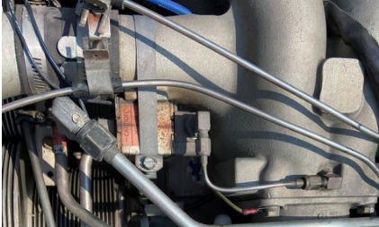Photograph 4 – View of the metered pressure test fitting at the accident site, with the protective cap not installed and blue staining present on the fitting, from the NTSB investigation of Piper PA46 accident near Radisson, Wisconsin, July 28, 2024
