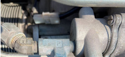 Photograph 5 – View of the metered pressure test fitting at the accident site, with the protective cap not installed and blue staining present on the fitting, from the NTSB investigation of Piper PA46 accident near Radisson, Wisconsin, July 28, 2024
