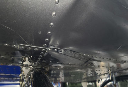 Photograph 6 – View of the substantial damage sustained to the front left underside of the fuselage inside of a hangar, from the NTSB investigation of Bell Helicopter Textron Canada 505 accident near Fort Worth, Texas, August 27, 2025