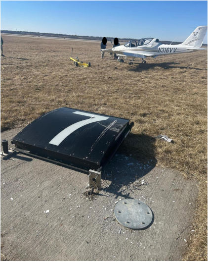 Photograph 2 – Taxiway sign impacted by left wing, from the NTSB investigation of Costruzioni Aeronautiche Tecna P-MENTOR accident near Des Moines, Iowa, February 11, 2026
