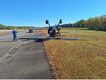 Photograph 1 – Front View of Airplane Inverted Next to the Runway, from the NTSB investigation of Boeing A75N1(PT17) accident near Williamsburg, Virginia, October 21, 2024