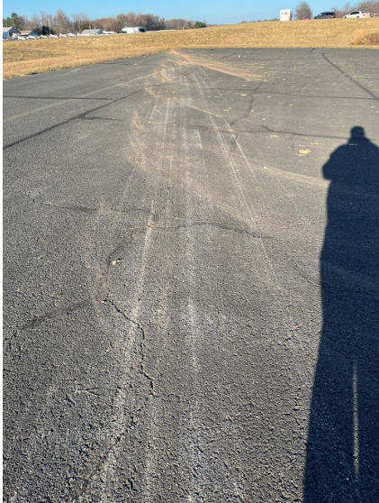 ON SCENE PHOTOGRAPHS Photograph 5 – Image of ground scars on the tarmac (looking toward runway), from the NTSB investigation of Beech A36 accident near Doylestown, Pennsylvania, November 18, 2024