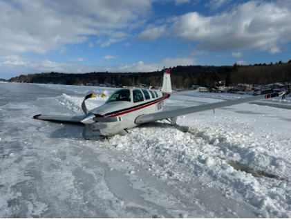 Photog rap h 1 – White airp lane with b lue and re d strip e s re sting on snowb ank (Courte sy of FAA), from the NTSB investigation of Beech A36 accident near Alton Bay, New Hampshire, February 23, 2025